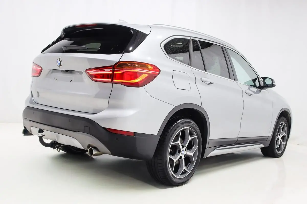 BMW X1 sDrive 18D argent métallisé vue 3/4 arrière droit avec attelage et toit ouvrant visible.