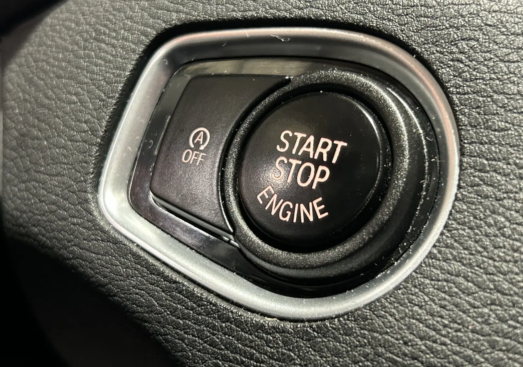 Gros plan sur le bouton noir Start Stop Engine entouré de cuir noir texturé dans une BMW X1 argent métallisé de 2019.