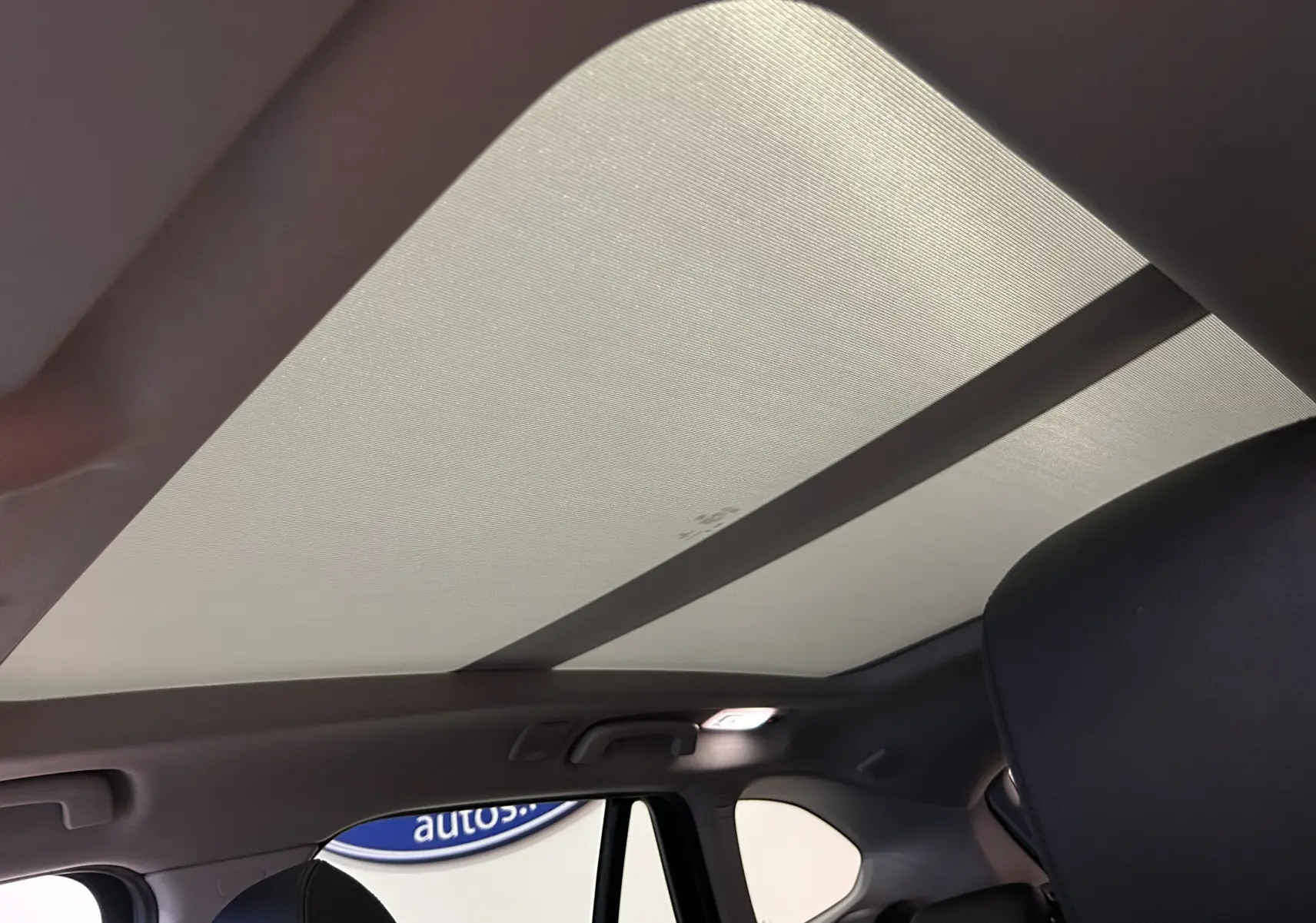 Vue intérieure du toit ouvrant fermé sur BMW X1 sDrive 18D argent métallisé, montrant la partie arrière des sièges noirs.