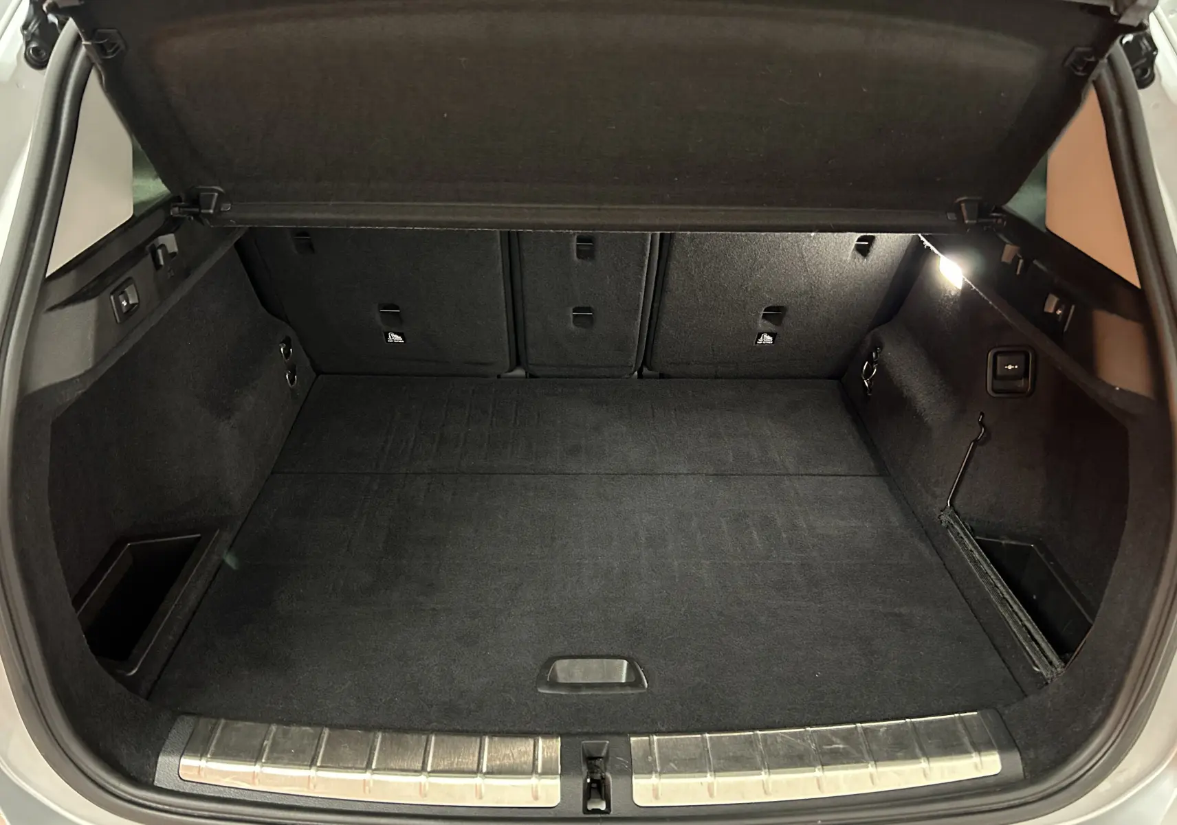 Coffre ouvert vu de l'arrière d'un BMW X1 argent métallique, montrant un espace de chargement propre et bien éclairé.