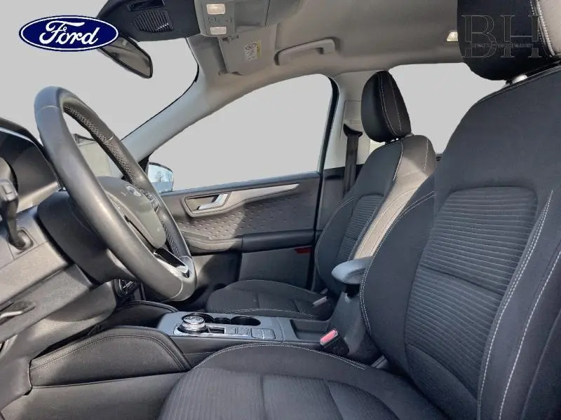 Vue intérieure côté conducteur du Ford Kuga 2020, sièges tissu noir avec surpiqûres blanches et volant cuir multifonction.