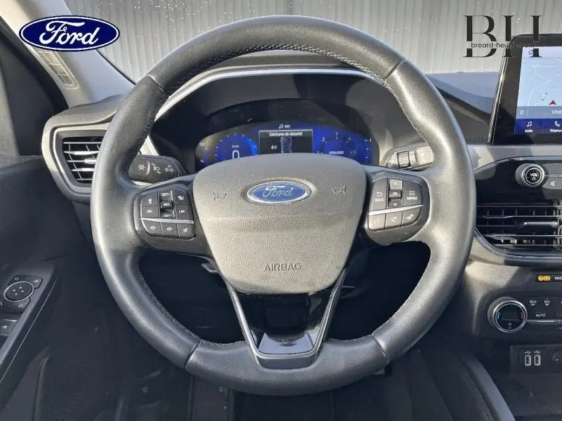 Vue rapprochée du volant cuir multifonction noir du Ford Kuga 2.0 EcoBlue 190ch avec tableau de bord digital et écran tactile.