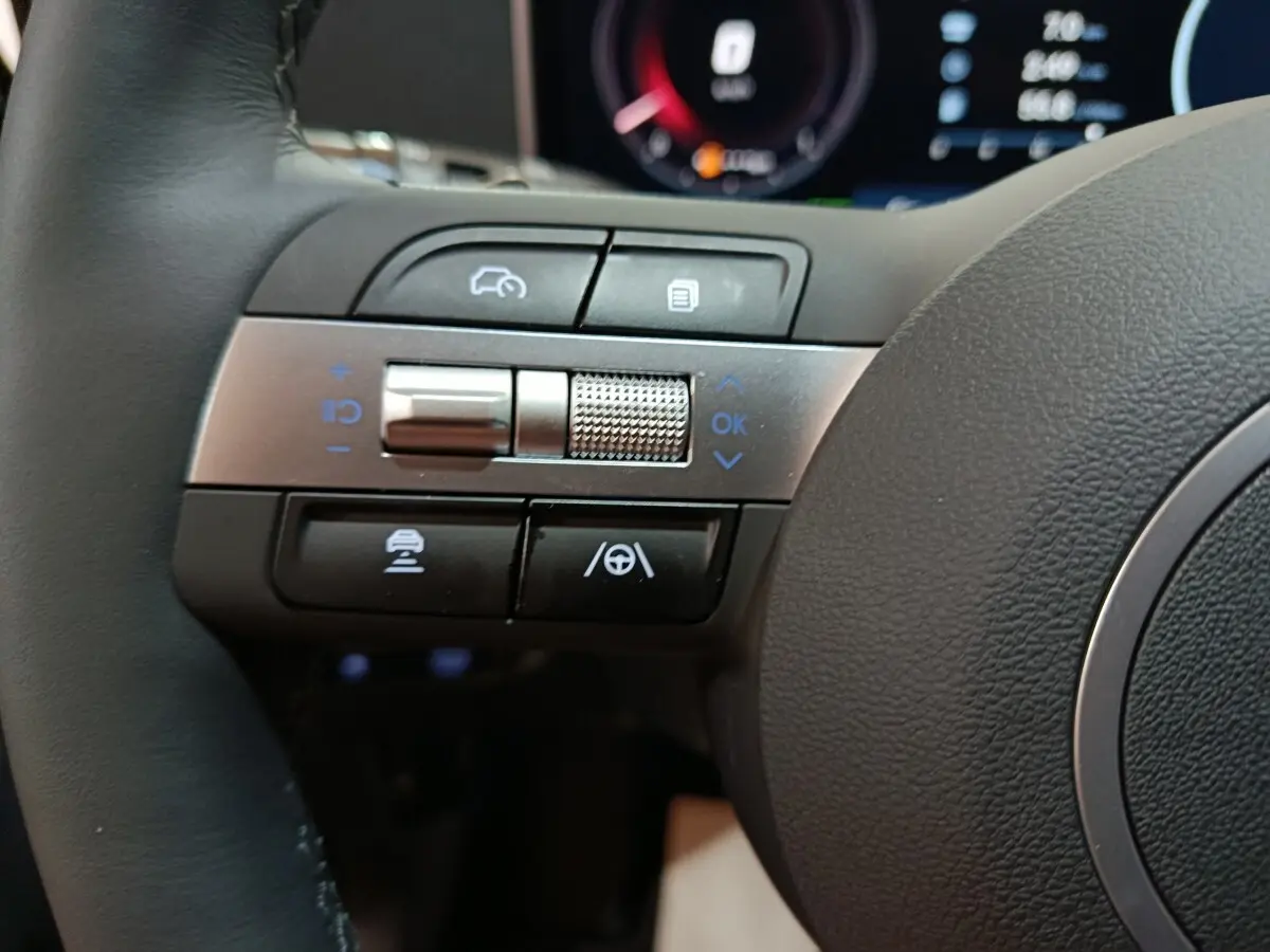 Gros plan sur les commandes multifonctions à gauche du volant du Hyundai Tucson 1.6 Hybrid 239 gris clair 2025.