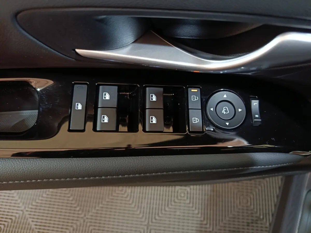 Gros plan sur les commandes de lève-vitres et rétroviseurs côté conducteur du Hyundai Tucson gris clair 2025 hybride.