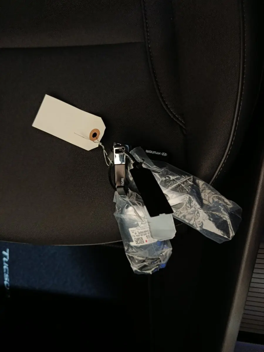 Clé de voiture Hyundai Tucson 1.6 Hybrid posée sur un siège tissu gris foncé à l'intérieur du véhicule.