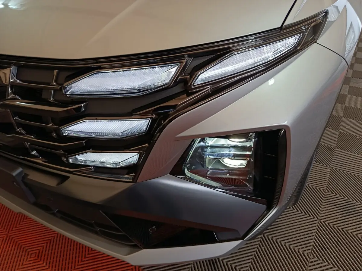 Gros plan sur le phare avant droit et la calandre noire du Hyundai Tucson gris clair 2025 hybride.