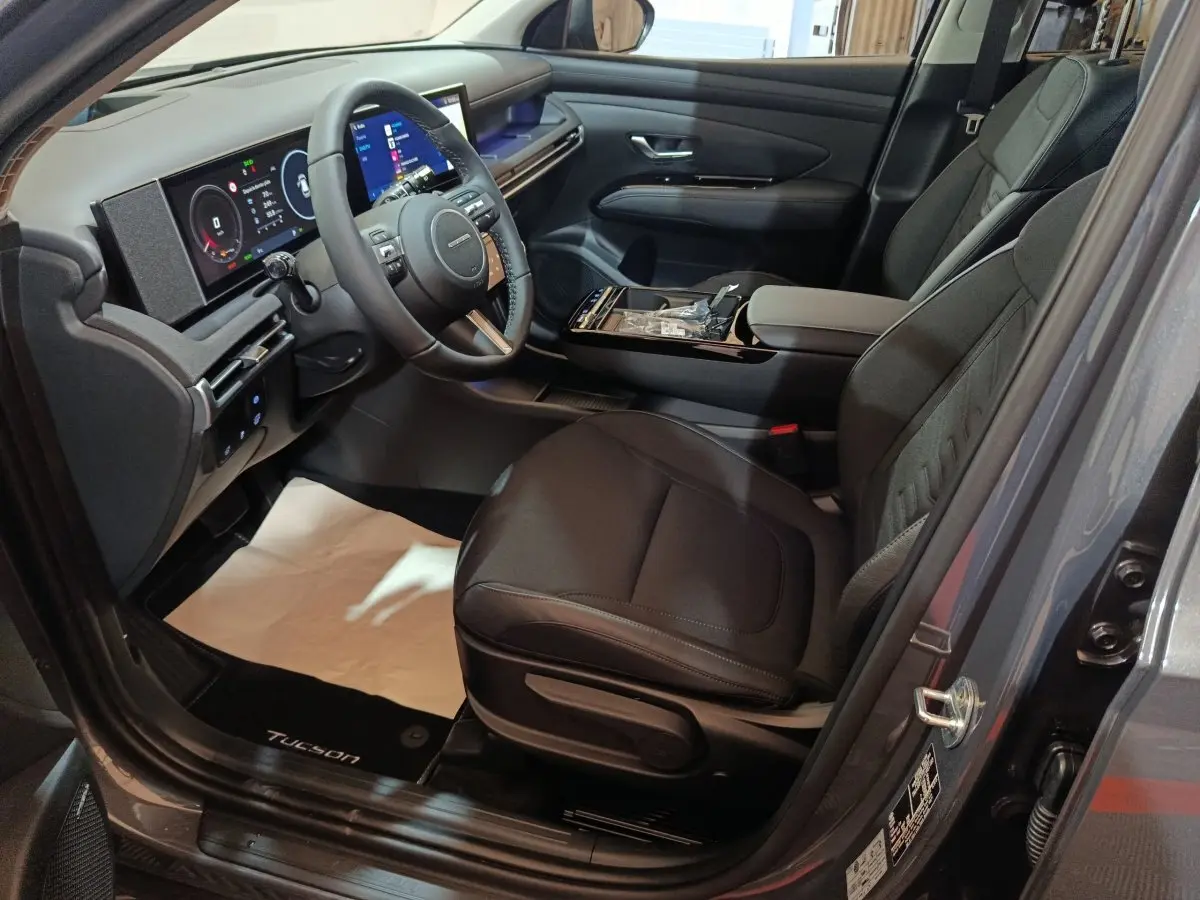 Vue intérieure côté conducteur du Hyundai Tucson gris clair 2025, avec tableau de bord numérique et sièges noirs.
