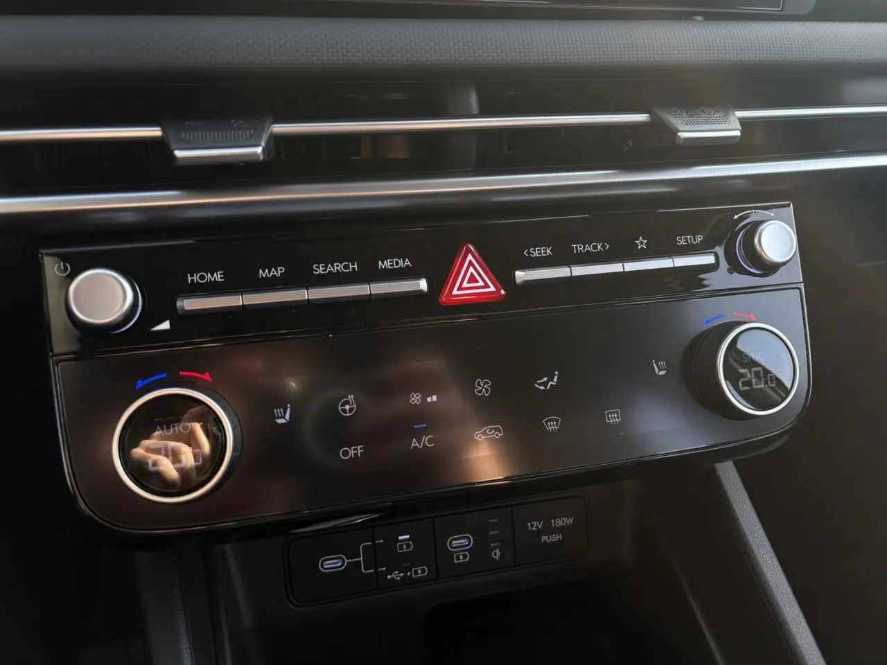 Gros plan sur la console centrale du Hyundai Tucson 2025, avec commandes climatisation et multimédia noires brillantes.