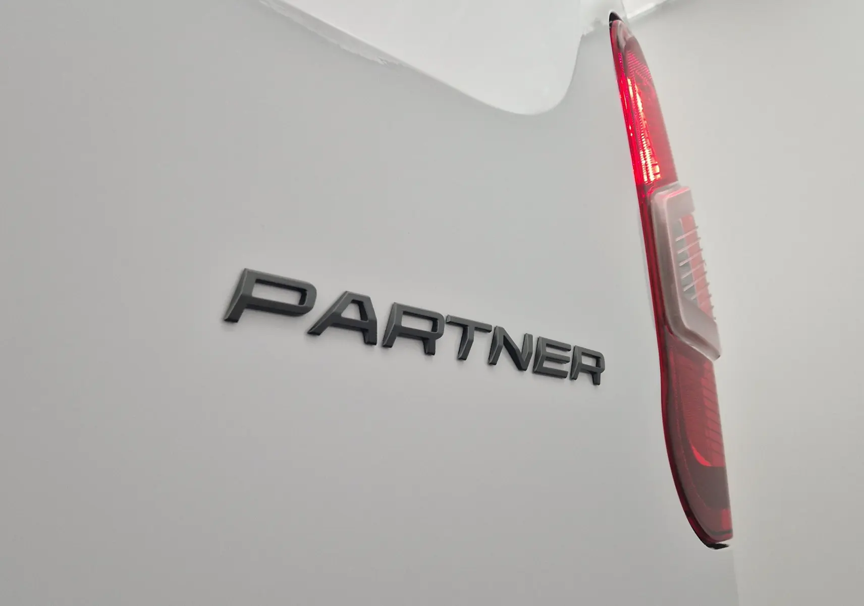Gros plan sur l'arrière blanc du Peugeot Partner avec le logo "PARTNER" et le feu arrière droit allumé.