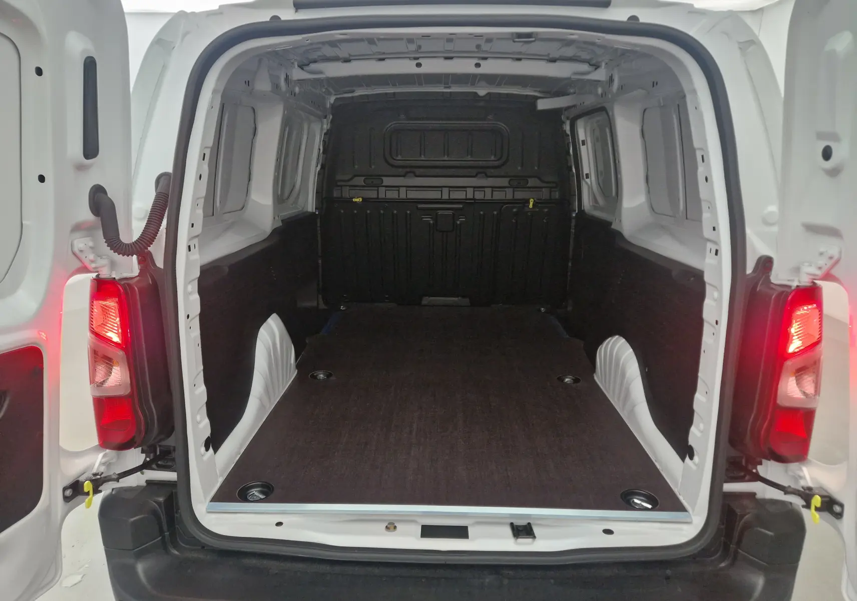 Vue arrière ouverte du Peugeot Partner blanc 2025, montrant l'espace de chargement avec plancher bois et parois protégées.