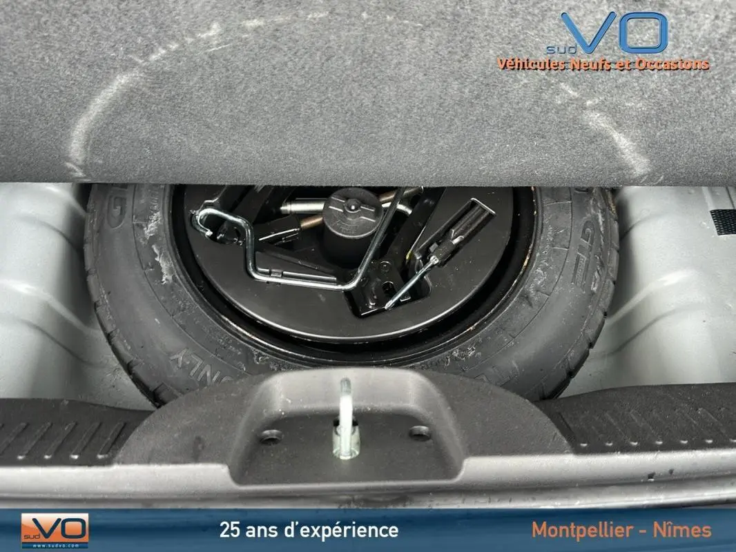 Gros plan sur la roue de secours noire et ses outils dans le coffre d'une FIAT 500C 2024 noire.