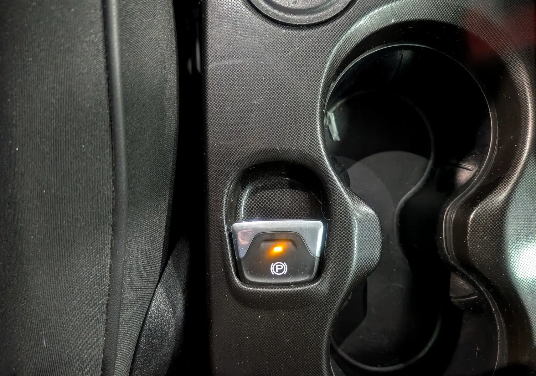 Gros plan sur le bouton de frein à main électrique allumé dans la console centrale d’une FIAT 500X Bleu Venezia 2024.