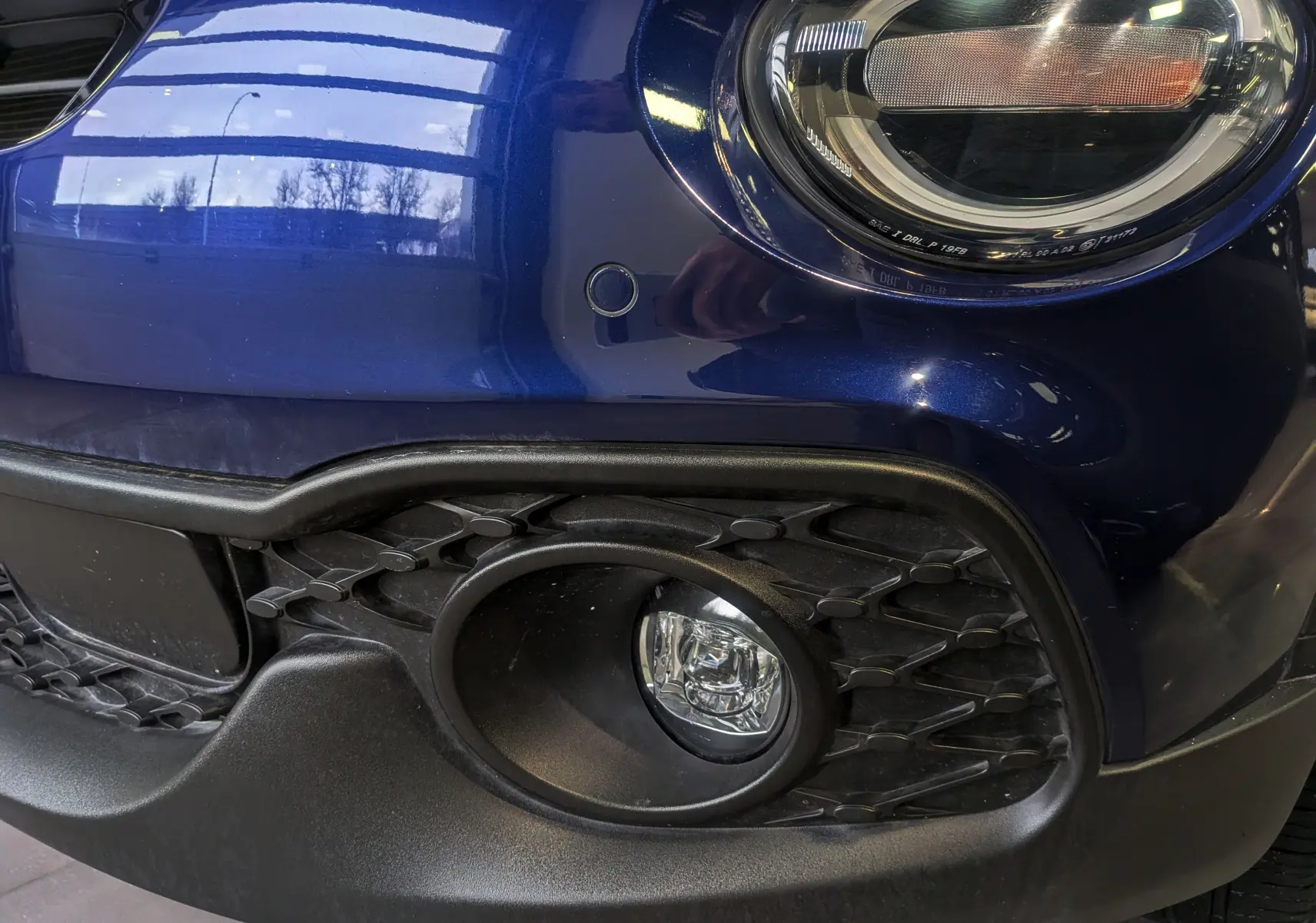 Gros plan sur le phare avant droit et le pare-chocs bleu Venezia du FIAT 500X 2024 avec antibrouillard intégré.