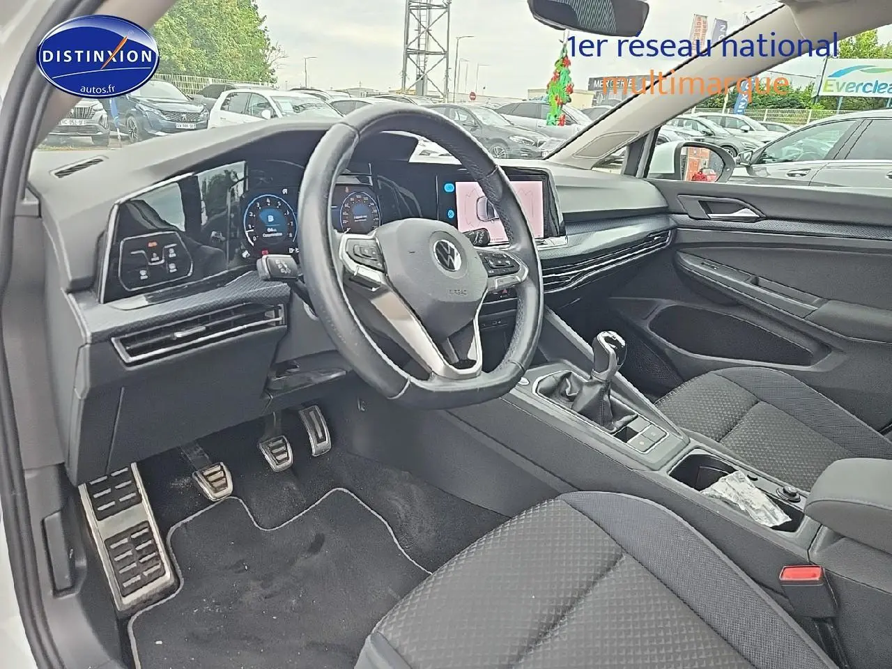 Vue intérieure côté conducteur de la Volkswagen Golf blanche, avec volant cuir multifonction et écran tactile central.