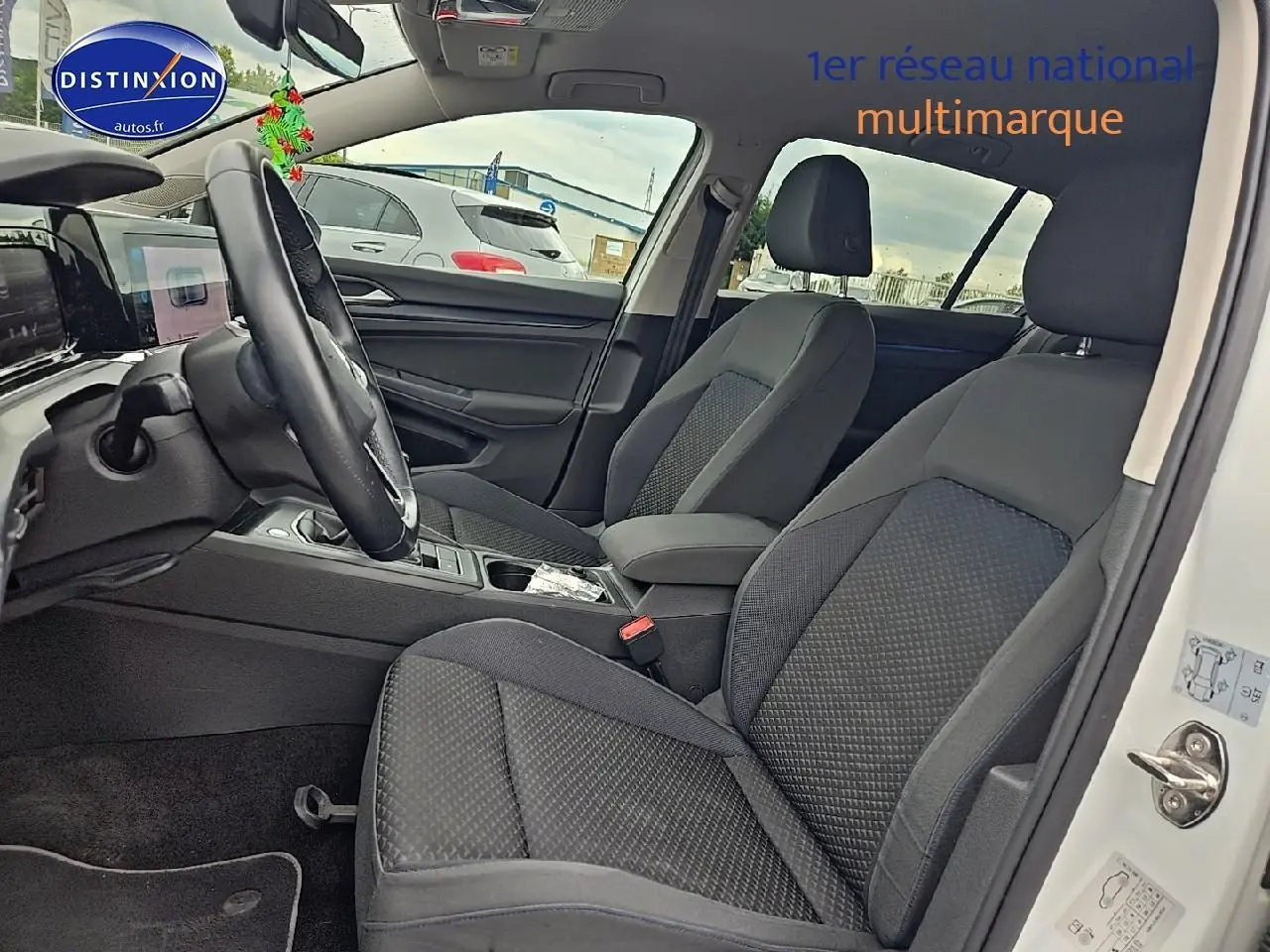 Vue intérieure côté conducteur de la Volkswagen Golf blanche 2021, sièges tissu gris et volant cuir multifonction.