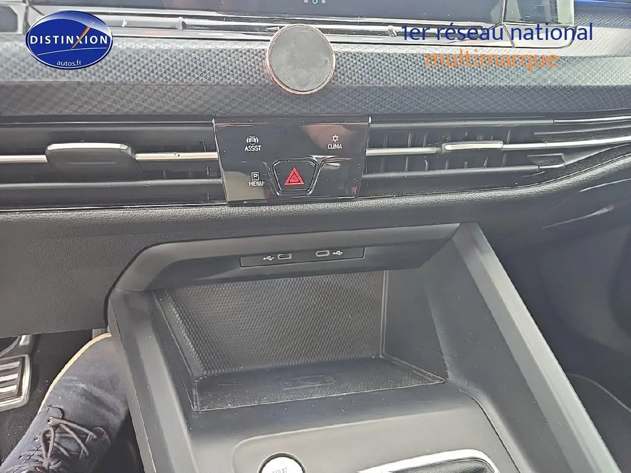 Vue rapprochée de la console centrale noire de la Volkswagen Golf 1.5 TSI essence, avec commandes d’assistance et climatisation.