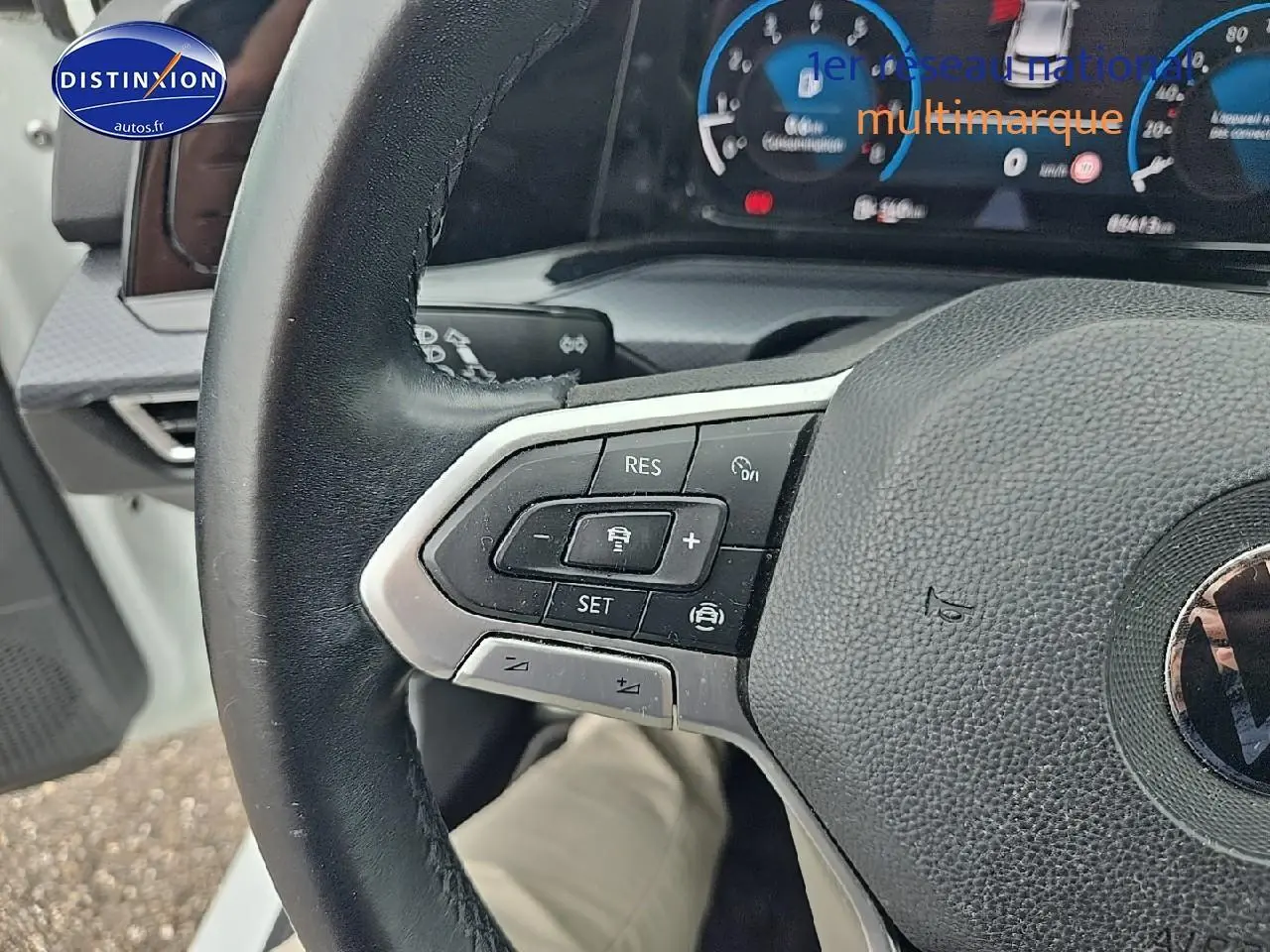 Gros plan sur le volant cuir multifonction noir de la Volkswagen Golf blanche, avec commandes de régulateur de vitesse visibles.