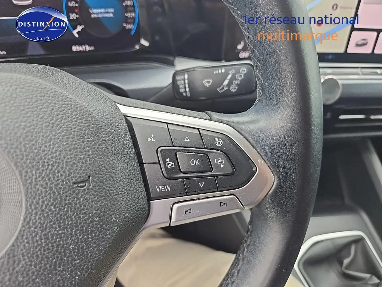 Gros plan sur le volant cuir noir multifonction côté gauche de la Volkswagen Golf blanche avec tableau de bord digital visible.