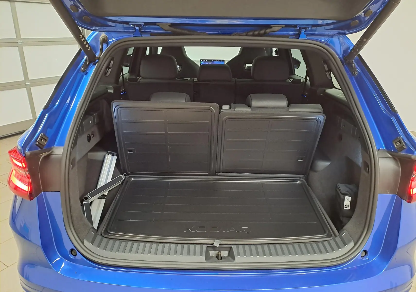 Coffre ouvert vu de l'arrière d'un Skoda Kodiaq Bleu RS 2025, montrant l'espace de chargement et les sièges arrière rabattus.