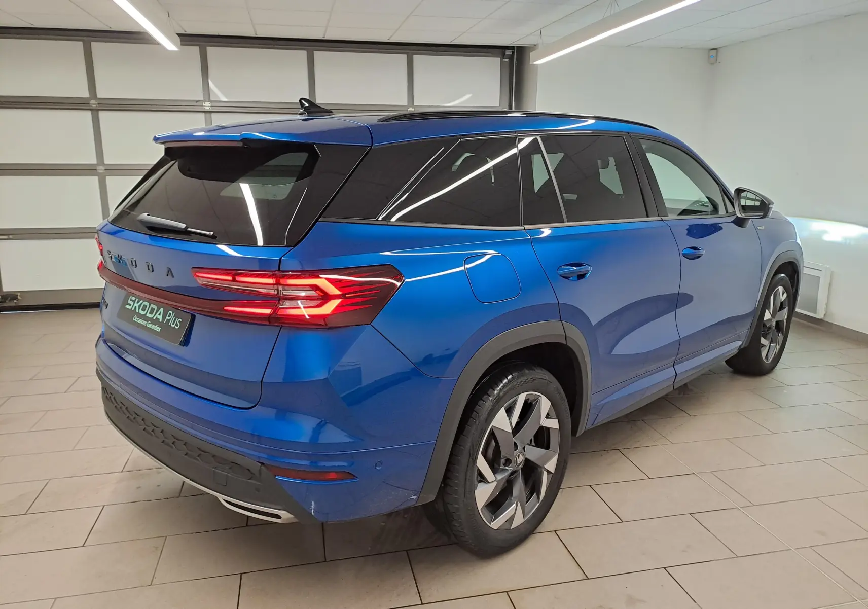 Vue 3/4 arrière droite du Skoda Kodiaq Bleu RS 2025 avec toit panoramique et feux arrière allumés.