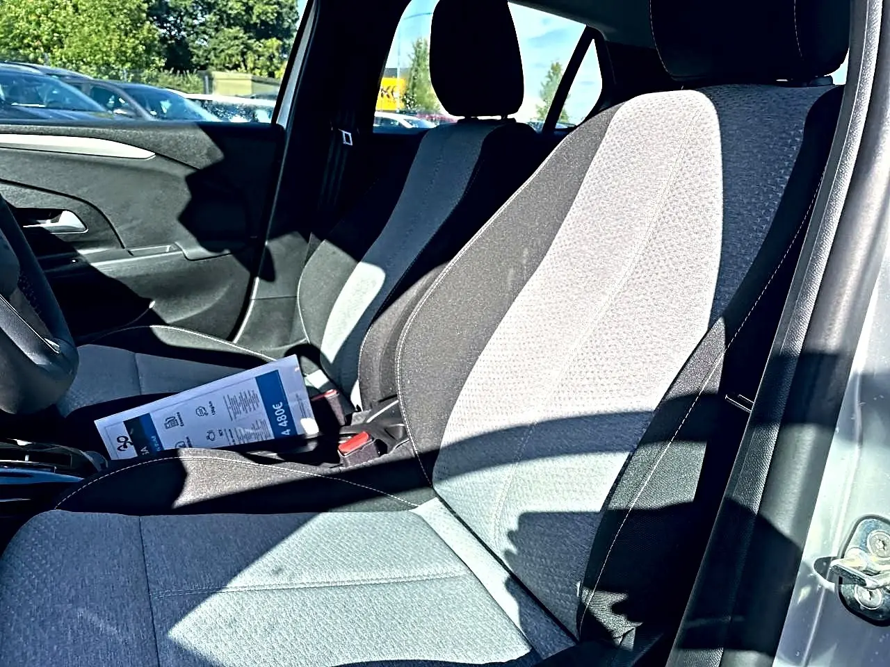 Vue intérieure côté conducteur de l’Opel Corsa gris 2025, sièges tissu bicolore noir et gris avec brochure posée dessus.