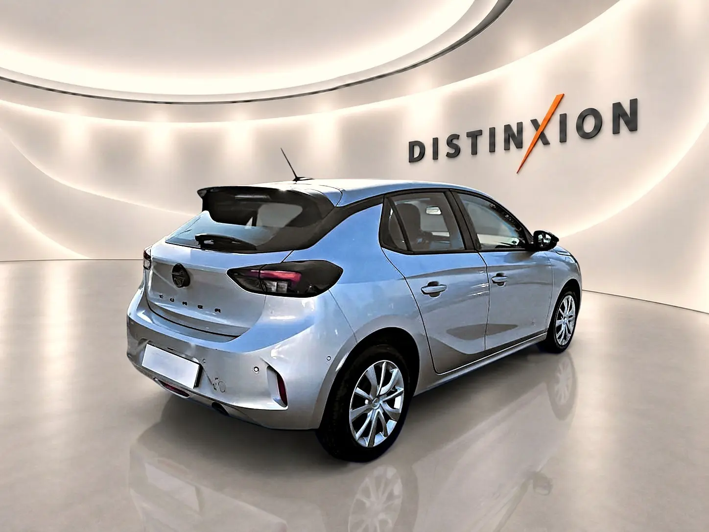 Opel Corsa gris 3/4 arrière droit en intérieur, avec toit noir et becquet arrière distinctif.