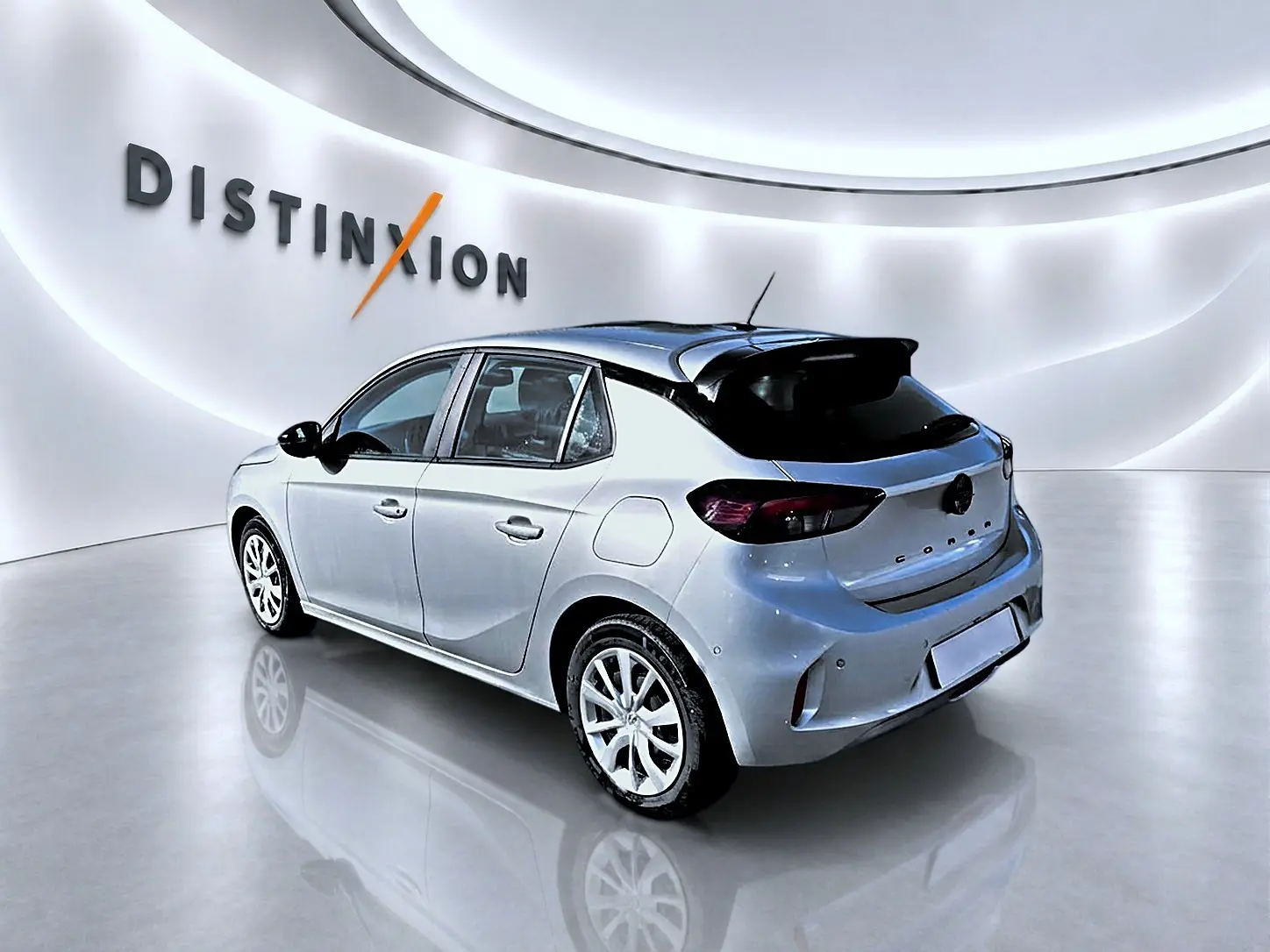 Opel Corsa gris vue 3/4 arrière droit en intérieur avec becquet et jantes alliage visibles.
