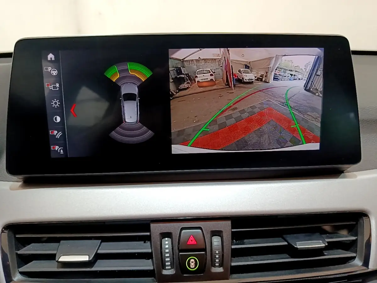 Écran multimédia montrant la caméra de recul et les capteurs de stationnement du BMW X1 blanc, vue intérieure.