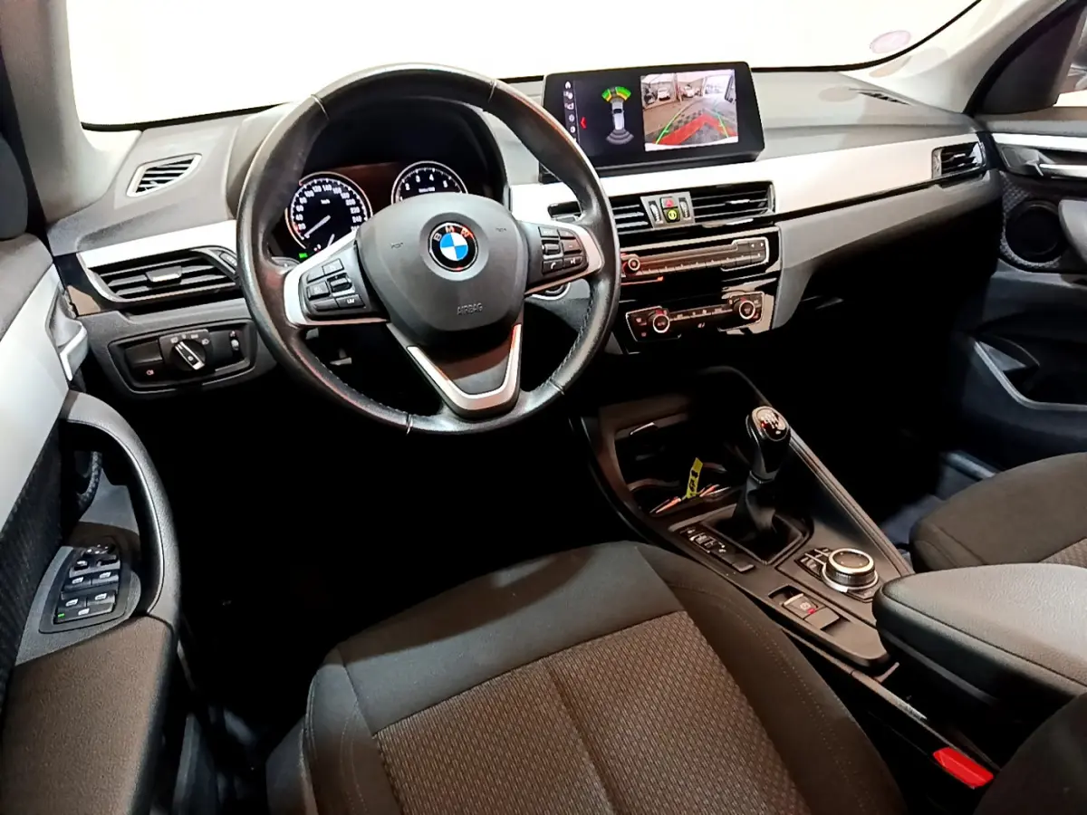 Vue intérieure avant de la BMW X1 sDrive18i Lounge 2019, volant cuir, écran multifonctions et levier de vitesses manuel.