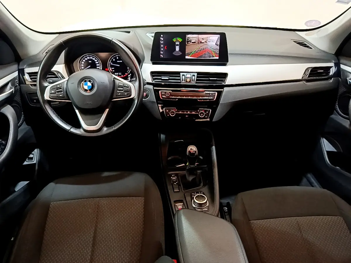 Vue intérieure avant du BMW X1 sDrive18i Lounge 2019, tableau de bord noir avec écran multimédia et volant cuir multifonctions.
