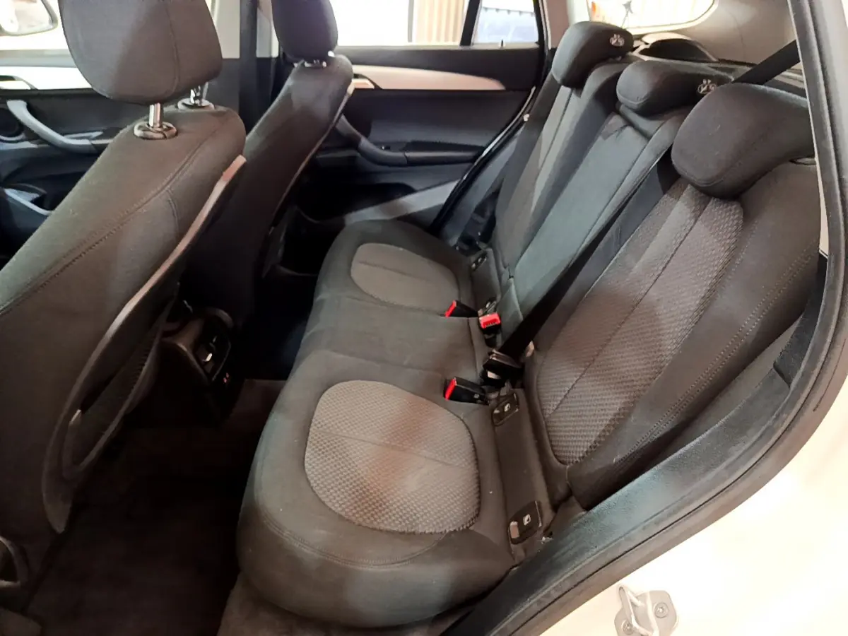 Vue intérieure arrière droite des sièges noirs du BMW X1 sDrive18i Lounge blanc de 2019, avec ceintures et appuie-têtes visibles.