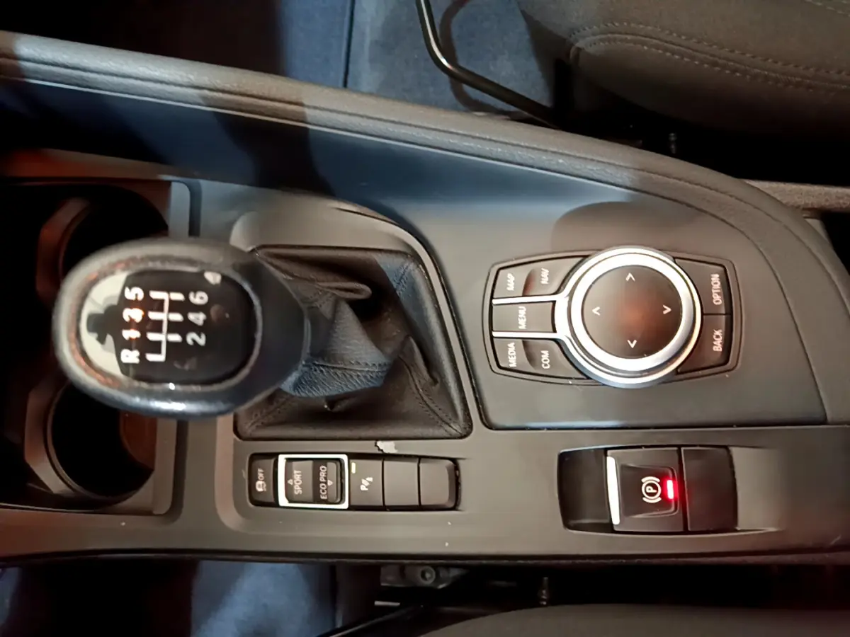 Vue plongeante sur la console centrale noire du BMW X1 sDrive18i 2019 avec levier de vitesse manuel et molette de contrôle.