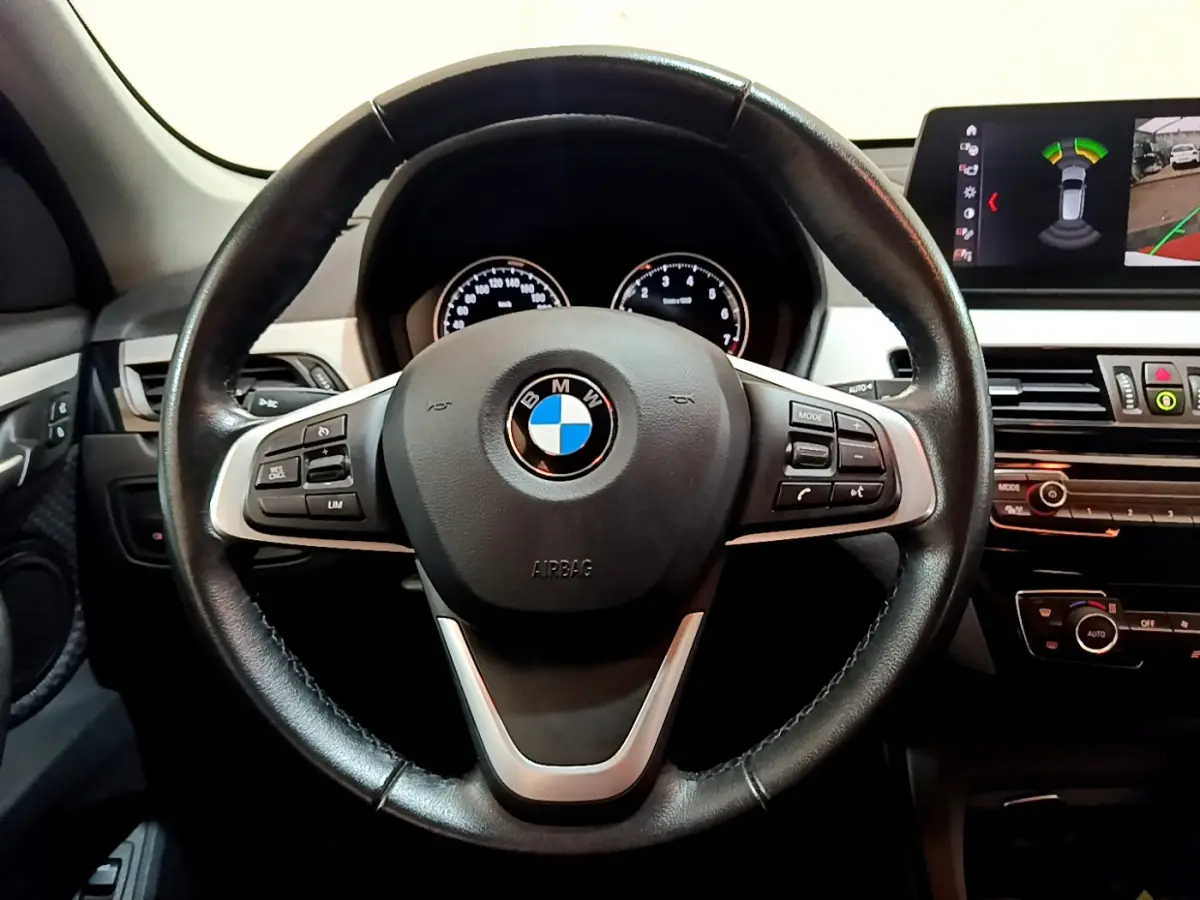 Vue rapprochée du volant cuir noir multifonctions et du tableau de bord digital d'une BMW X1 sDrive18i Lounge 2019.