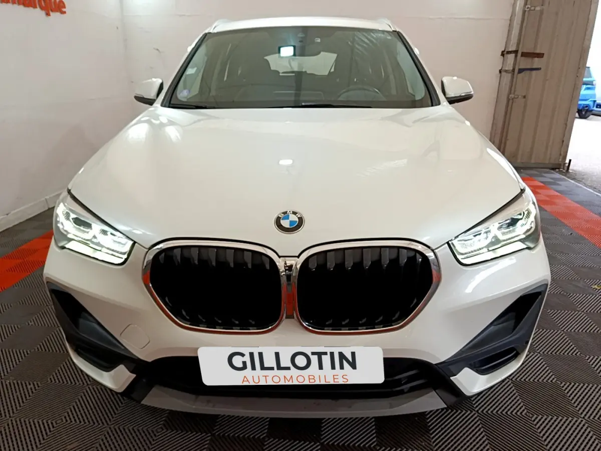 Vue frontale d'un BMW X1 sDrive18i Lounge blanc avec phares LED allumés et calandre noire distinctive.