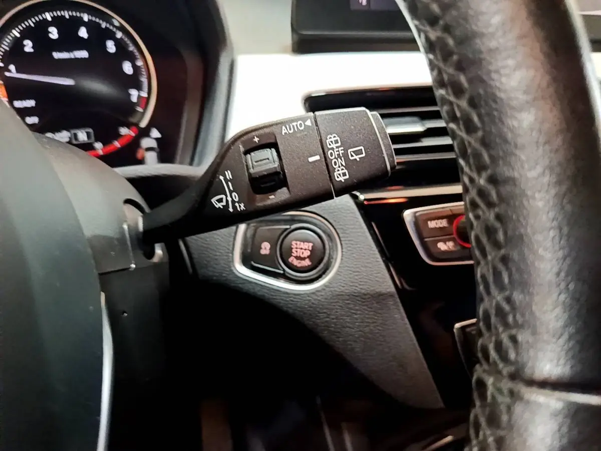 Gros plan sur la manette d’essuie-glace et le bouton start/stop du tableau de bord d’une BMW X1 blanche, intérieur noir.