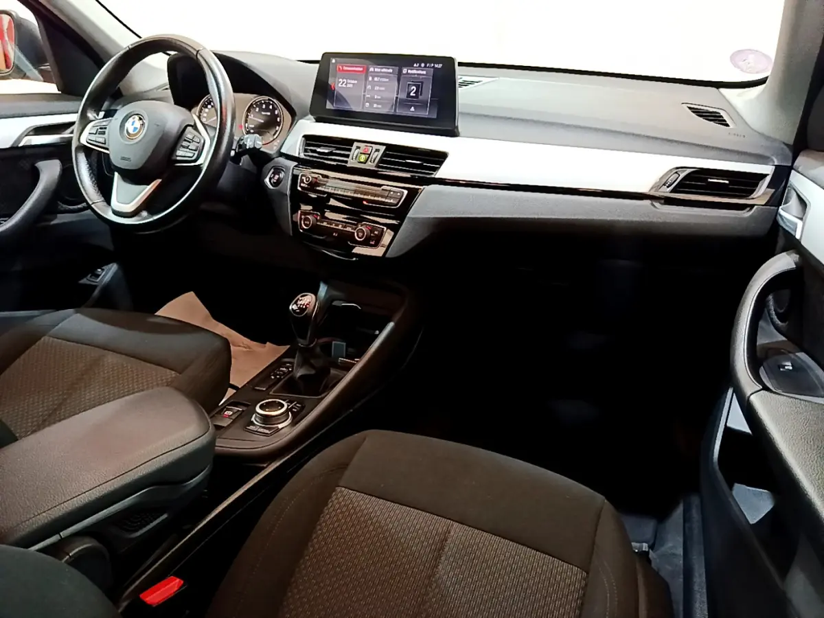 Intérieur avant droit de BMW X1 sDrive18i 2019, tableau de bord noir avec écran central et levier de vitesse manuel.