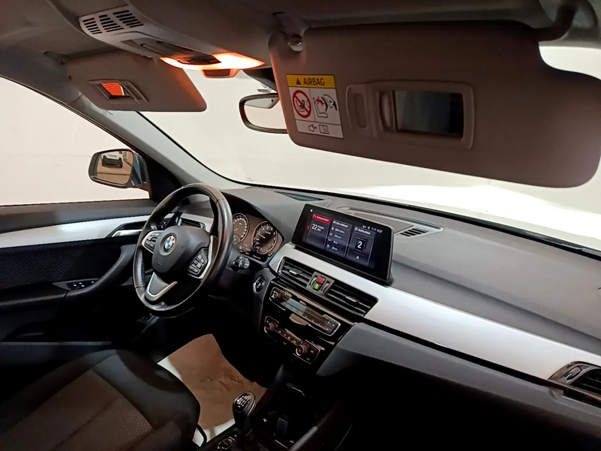 Vue intérieure côté conducteur du BMW X1 blanc 2019, volant cuir multifonctions et écran central 6,5 pouces.