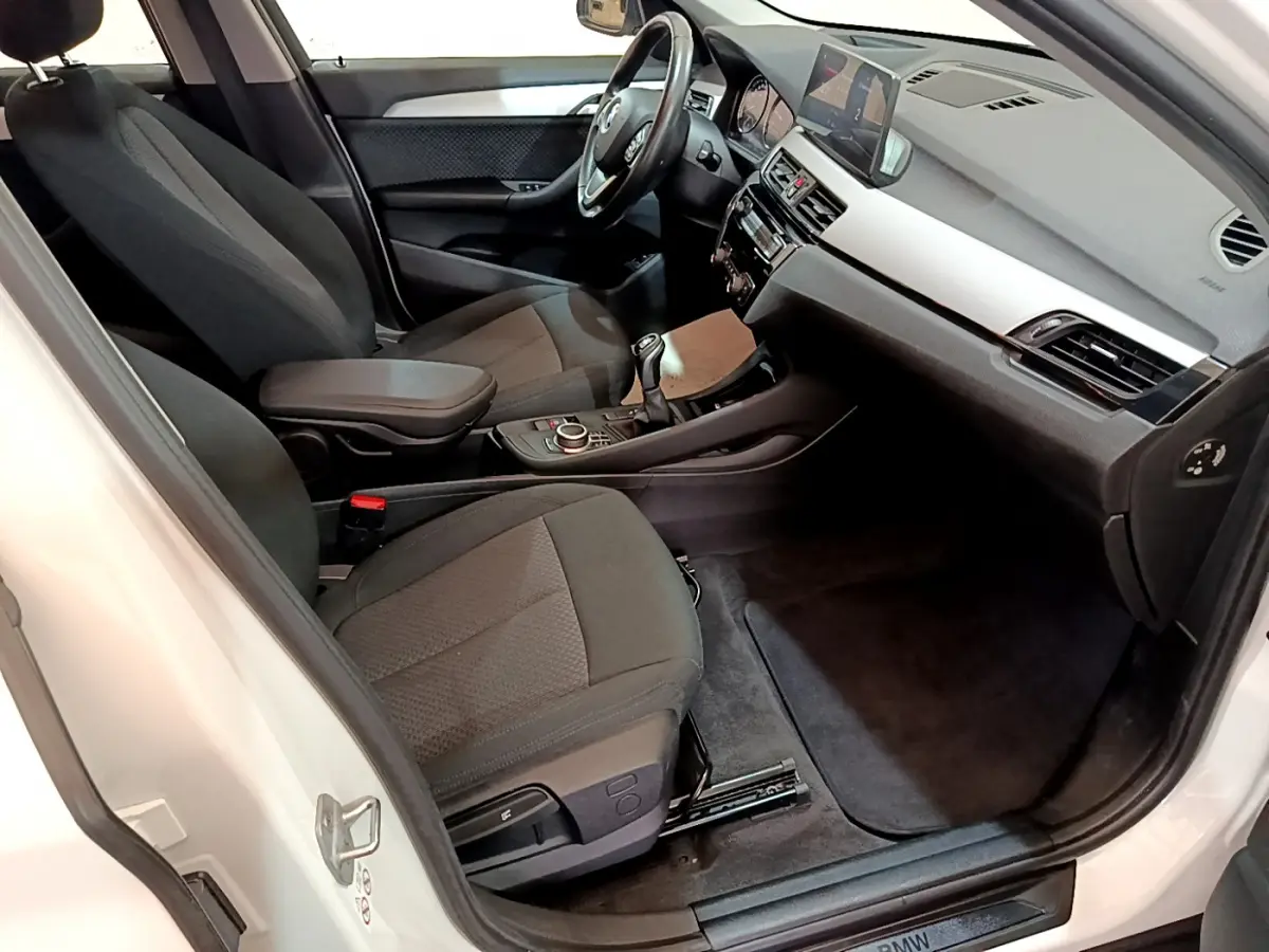 Vue intérieure côté conducteur de la BMW X1 sDrive18i Lounge 2019, sièges noirs et tableau de bord moderne.