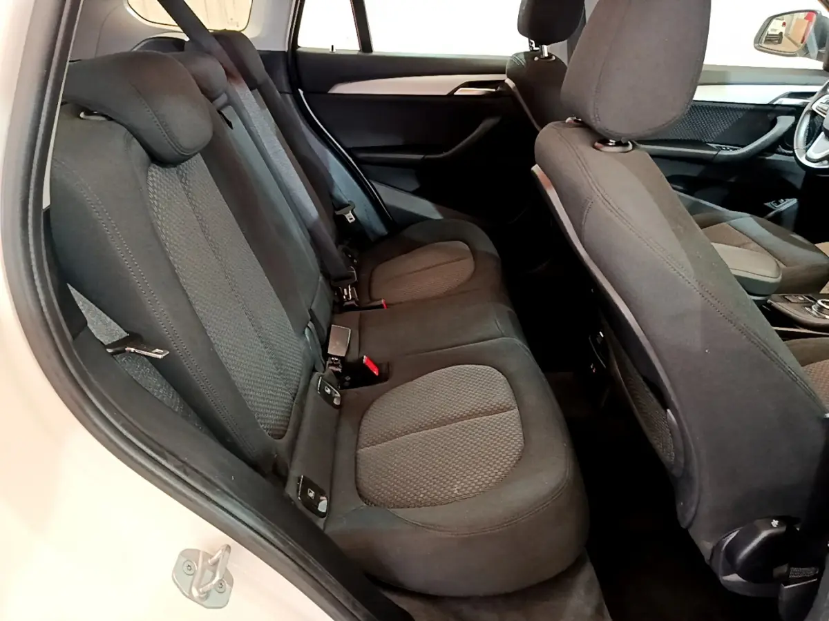 Vue intérieure côté gauche sur les sièges arrière noirs et le dossier avant du BMW X1 sDrive18i Lounge blanc.