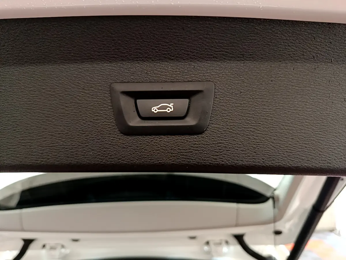 Bouton d'ouverture électrique du coffre sur la partie intérieure du hayon arrière blanc d'un BMW X1 sDrive18i Lounge.