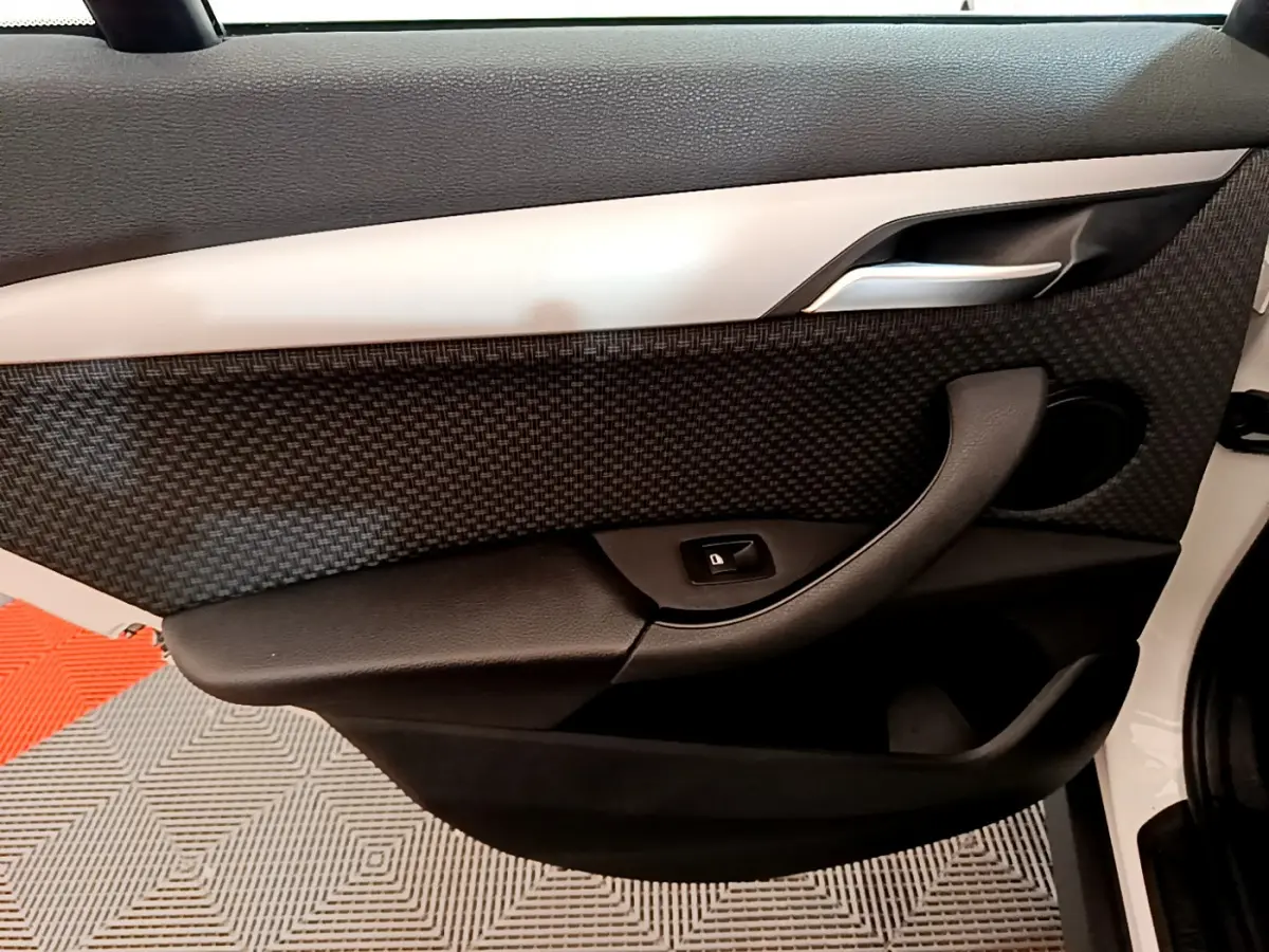 Vue intérieure du panneau de porte avant droit du BMW X1 sDrive18i Lounge blanc, avec insert texturé et commande de lève-vitre.