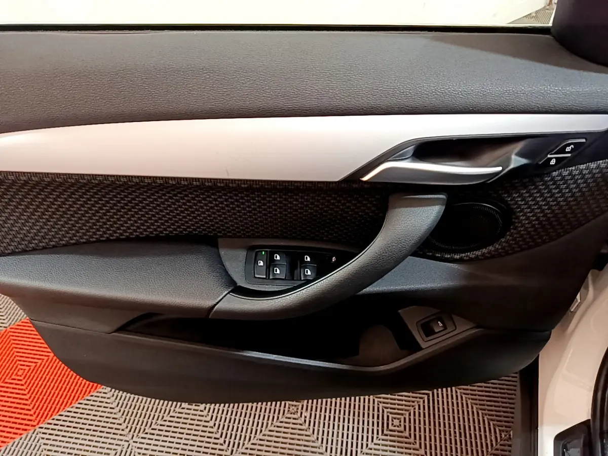 Vue intérieure du panneau de porte côté conducteur du BMW X1 blanc, avec commandes de vitres et poignée argentée.