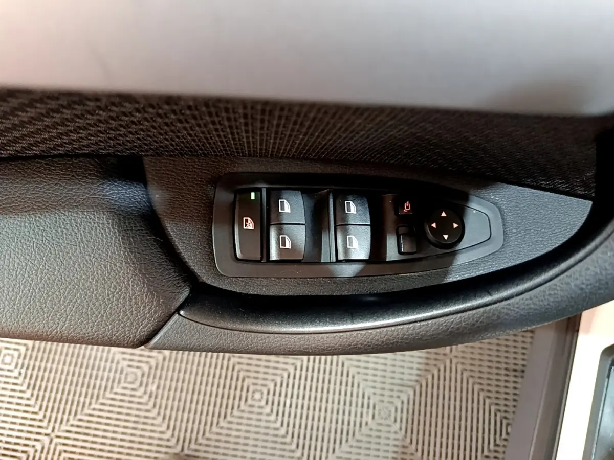 Gros plan sur les commandes de lève-vitres et rétroviseurs côté conducteur du BMW X1 blanc sDrive18i Lounge 2019.