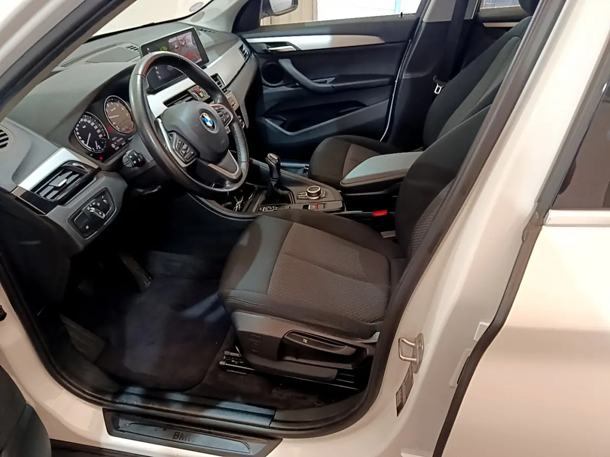 Intérieur côté conducteur d'une BMW X1 sDrive18i blanche, montrant le volant cuir et la boîte manuelle.