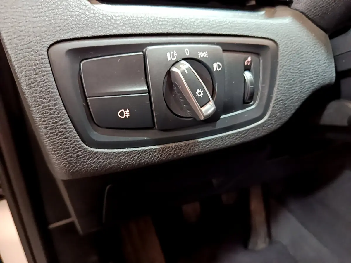 Gros plan sur le bouton de commande des phares noir dans l'habitacle du BMW X1 sDrive18i Lounge blanc.