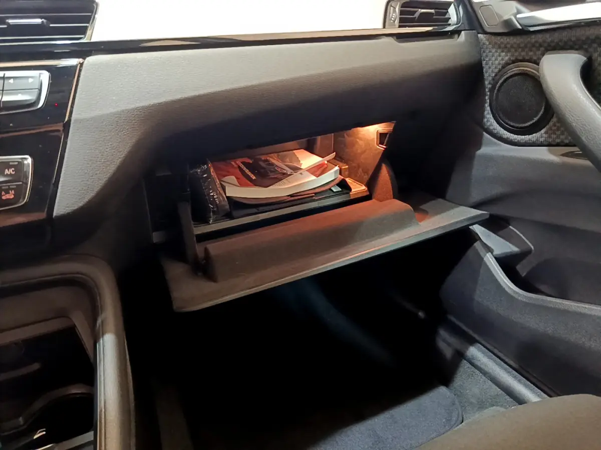 Gros plan sur la boîte à gants ouverte côté passager de la BMW X1 sDrive18i Lounge 2019 avec éclairage intérieur.