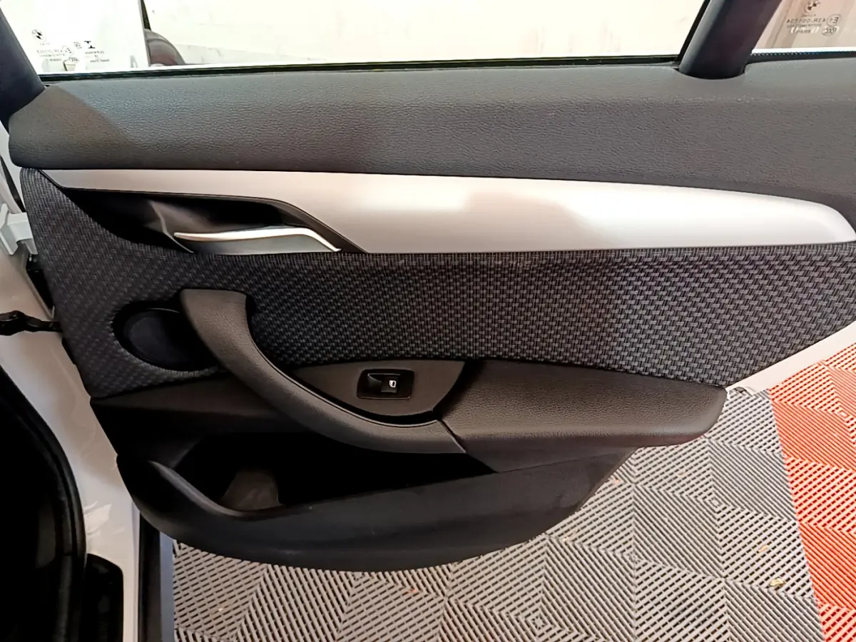 Vue intérieure côté gauche de la porte avant d’un BMW X1 sDrive18i Lounge blanc avec garniture tissu et plastique noir.