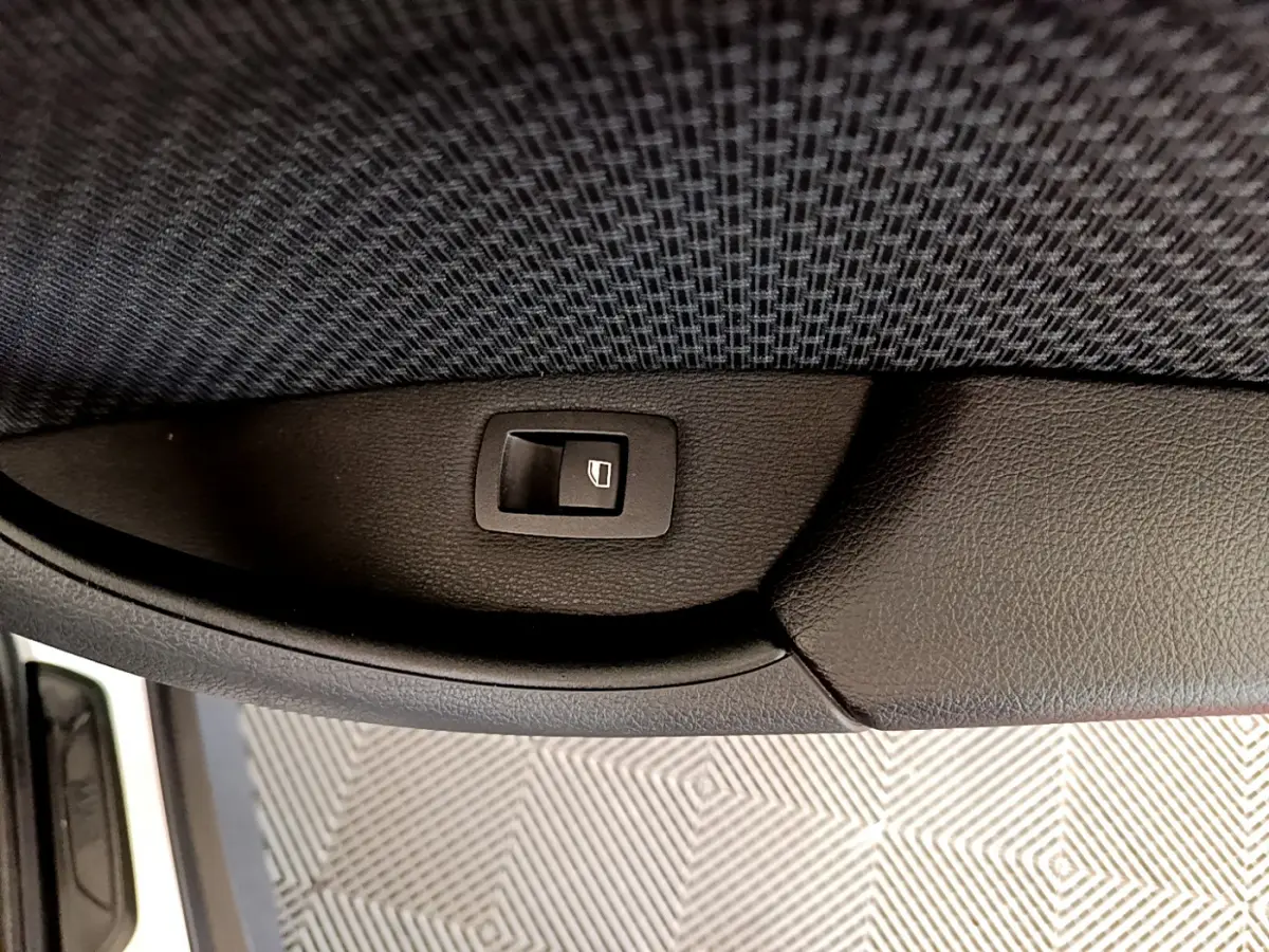 Bouton de commande de lève-vitre sur la porte intérieure côté conducteur d'une BMW X1 blanc, vue rapprochée.