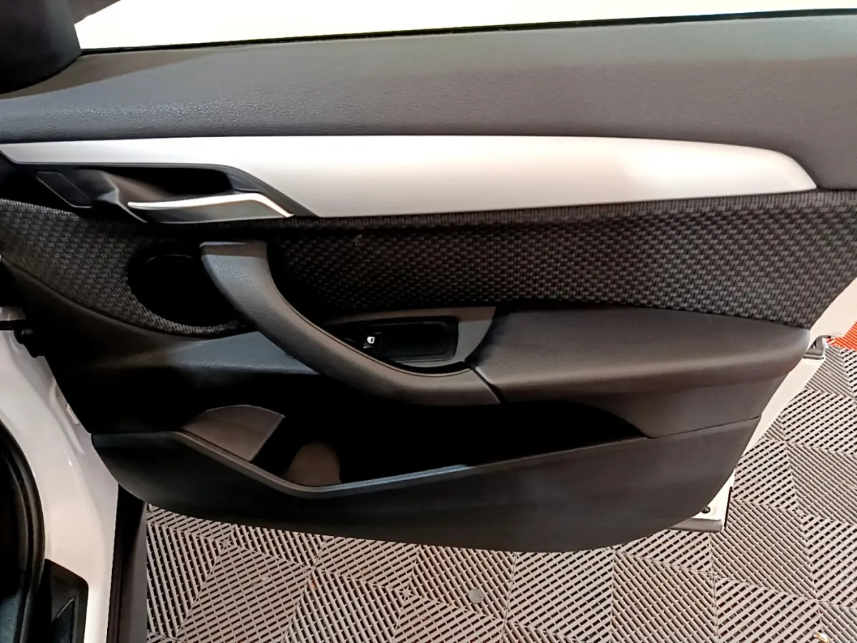 Détail de la porte avant gauche de la BMW X1 sDrive18i Lounge blanche, avec garniture noire texturée et poignée intégrée.