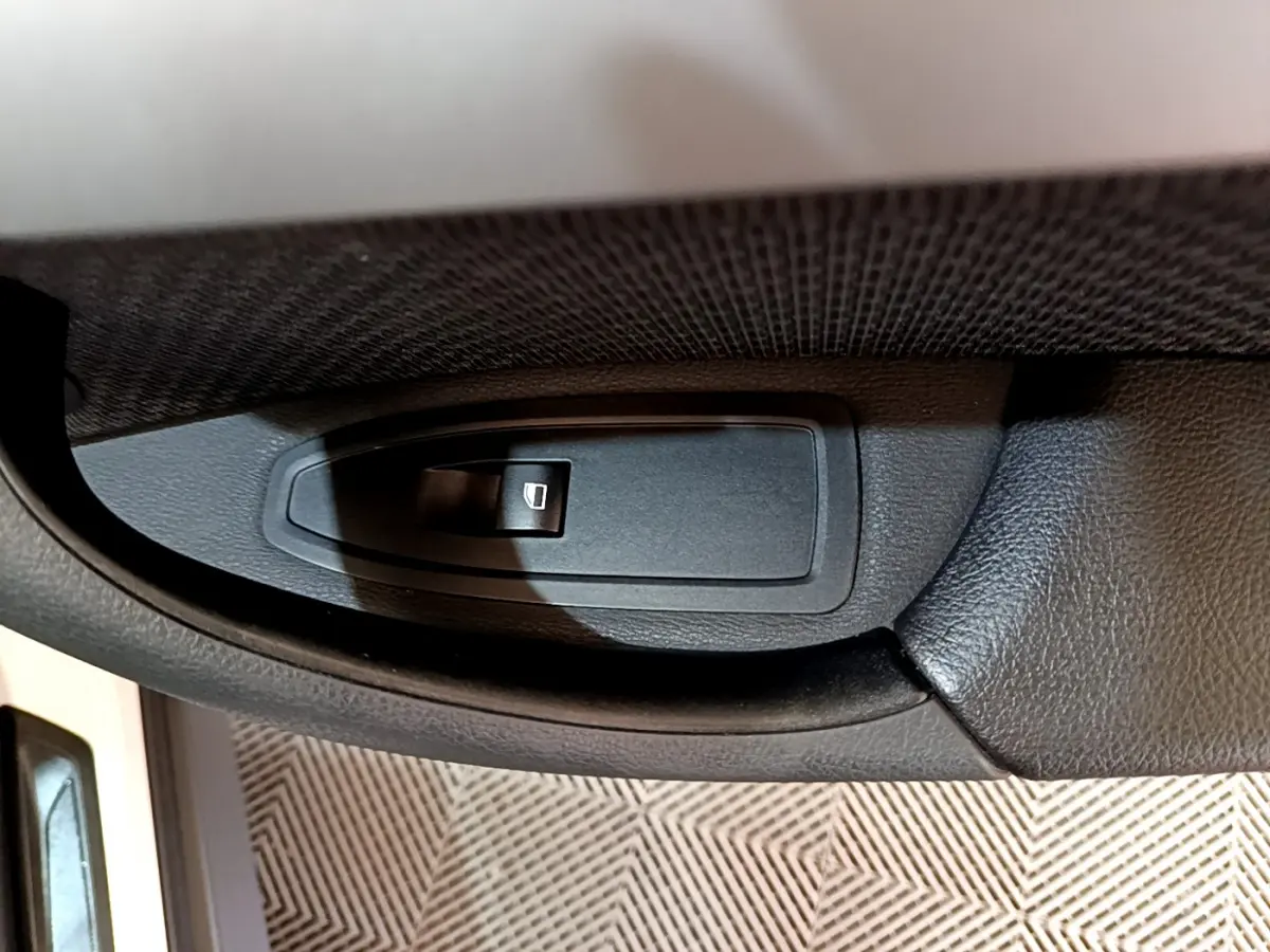 Gros plan sur le bouton de lève-vitre électrique côté conducteur d'une BMW X1 sDrive18i Lounge blanche.
